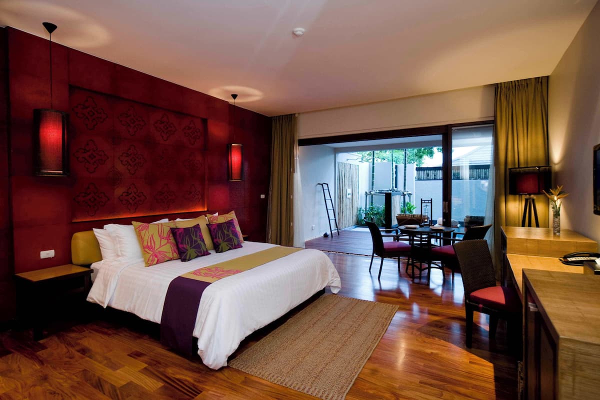 A hotel room with a large bed, a dining area, and a view of the outdoors.