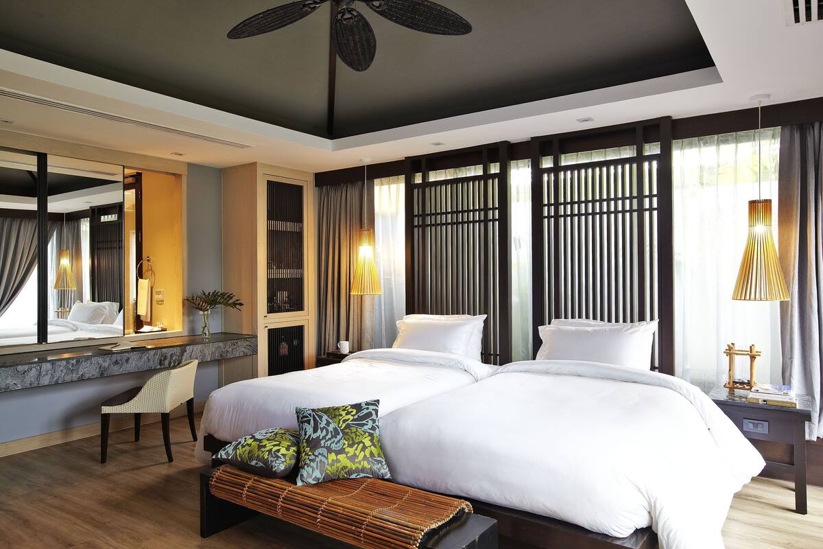 A hotel room with a large bed, a desk, a chair, and a window with curtains.