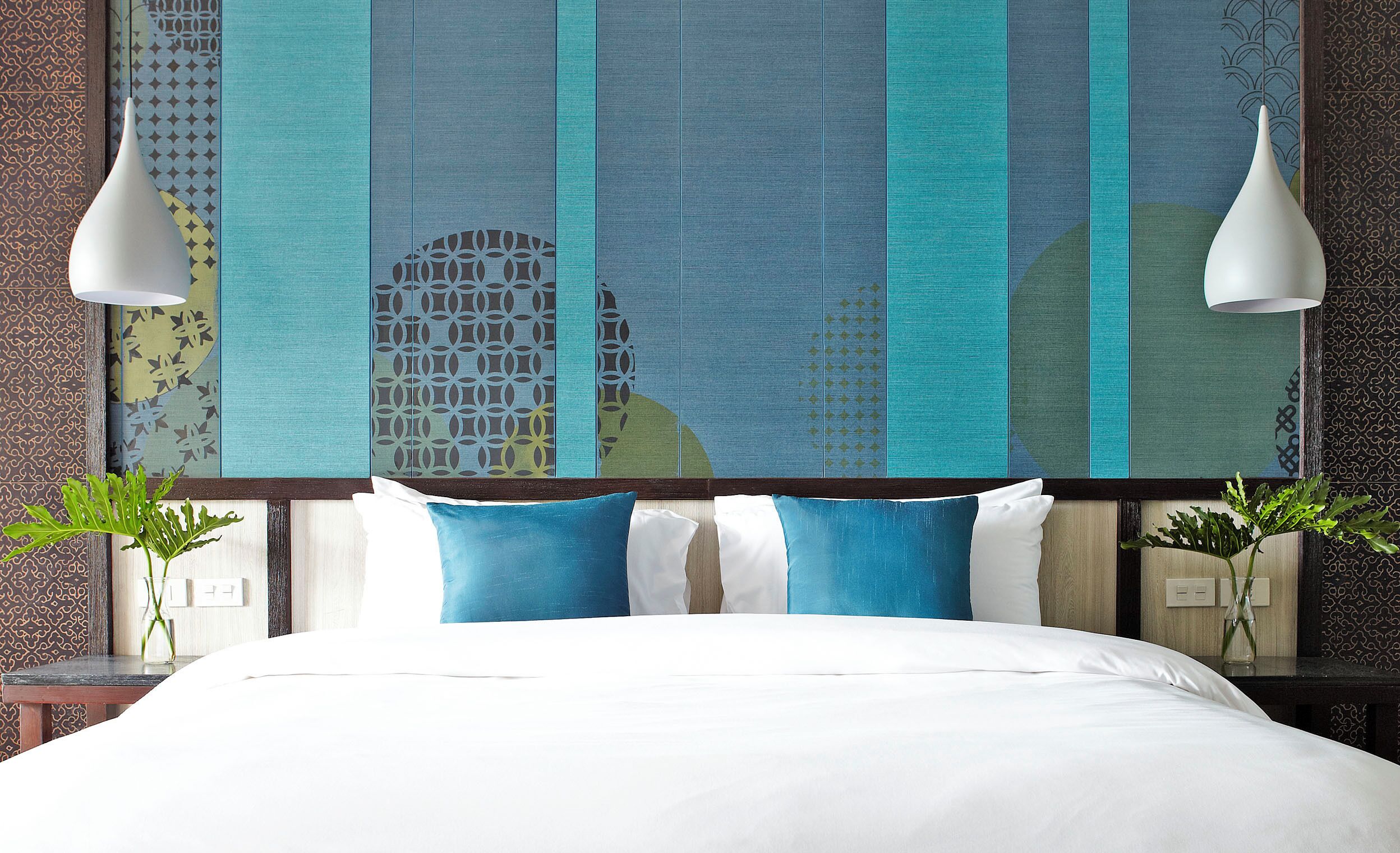 A bed with white bedding, blue and white pillows, and a decorative wall with a geometric pattern.