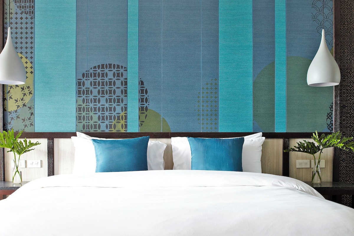 A bed with white bedding, blue and white pillows, and a decorative wall with a geometric pattern.