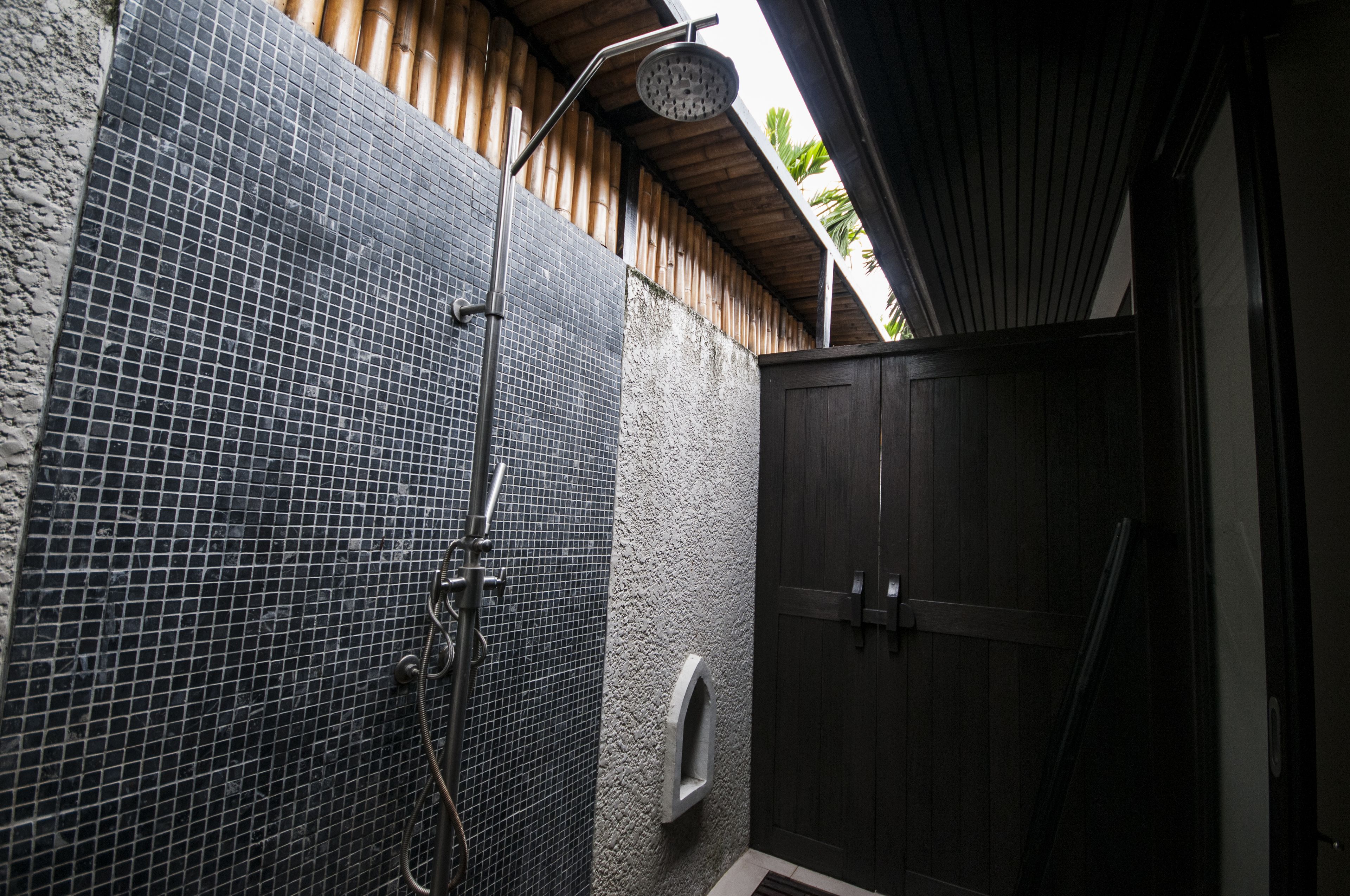Zona de ducha con pared de azulejos, puerta de madera y cabezal de ducha metálico.