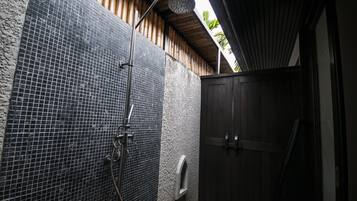 Zona de ducha con pared de azulejos, puerta de madera y cabezal de ducha metálico.