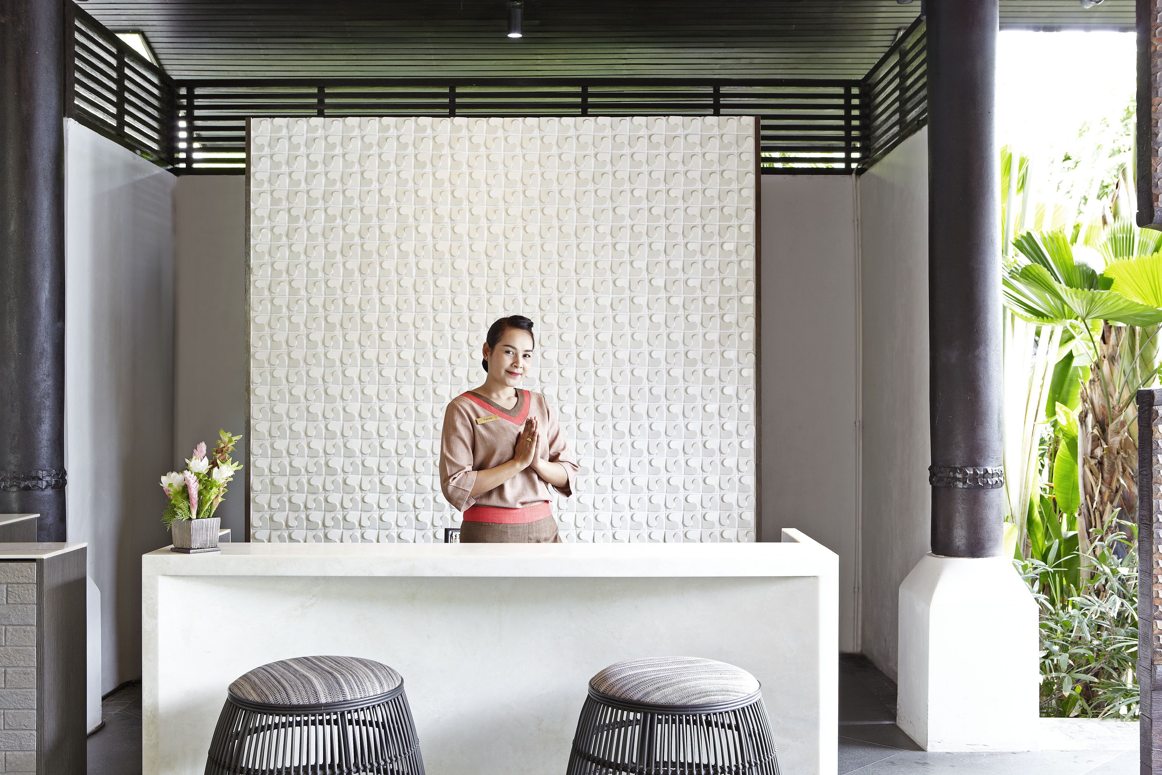 A reception area with a white reception desk, two wicker stools, a potted plant, and a textured wall.