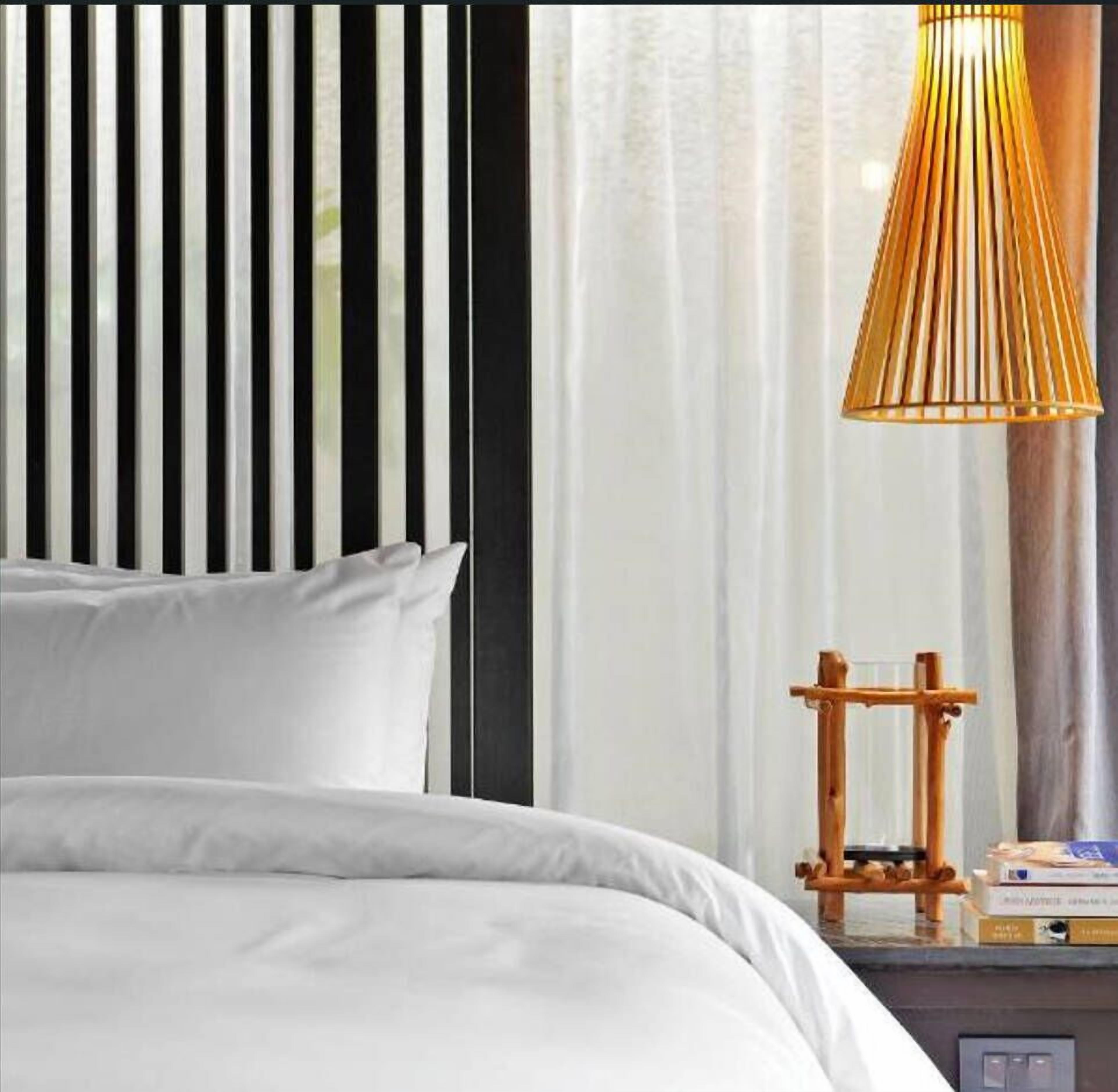 A bed with white bedding, a wooden nightstand with a lamp, and a window with curtains.