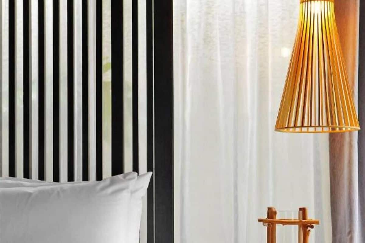A bed with white bedding, a wooden nightstand with a lamp, and a window with curtains.