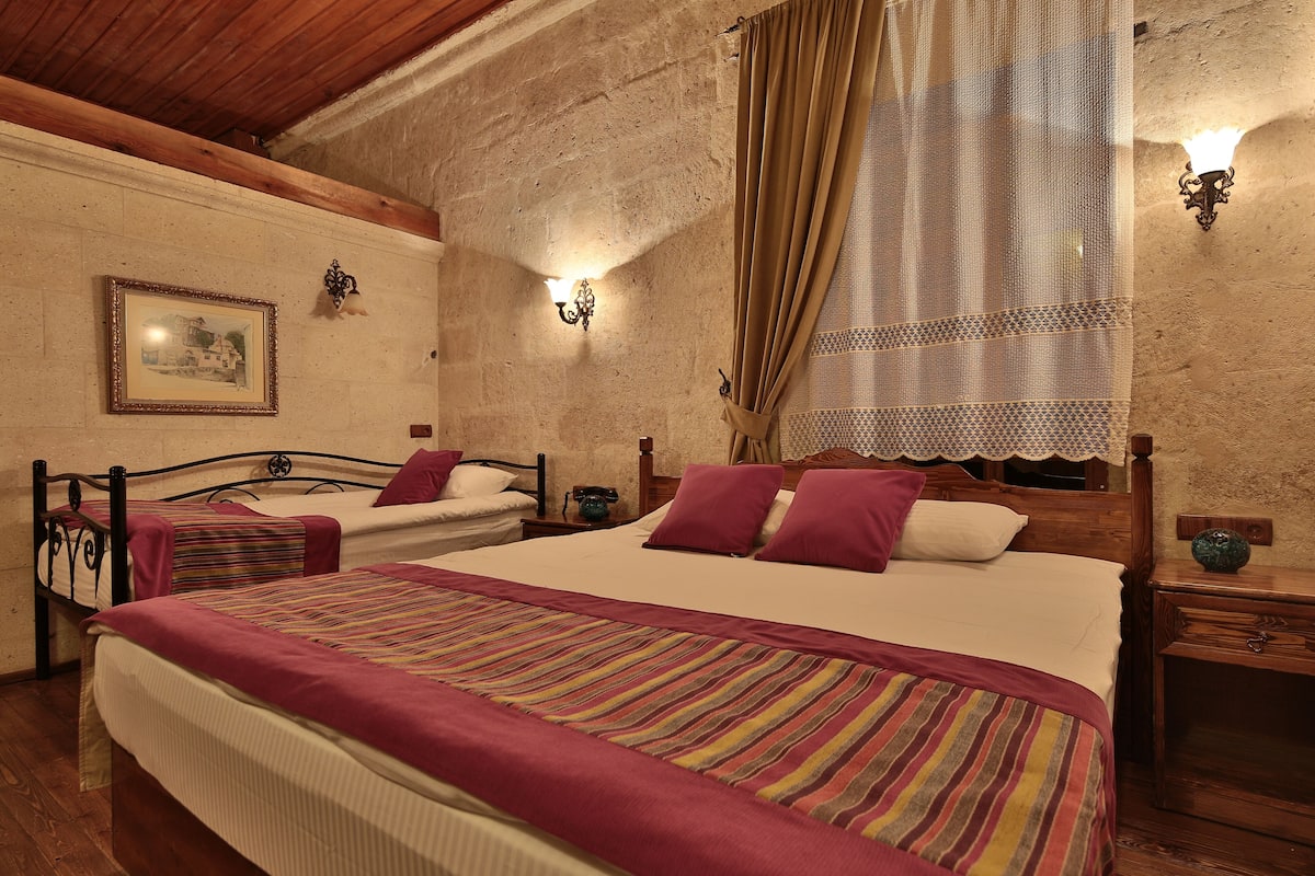 A bedroom with two beds, a wooden ceiling, a stone wall, and a picture on the wall.