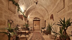 An arched hallway with stone walls, a patterned rug, and potted plants. - Elif Stone House (Ürgüp)