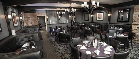 A restaurant with round tables, black leather booths, and a patterned carpet.