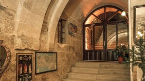 A stone staircase leading to a grand arched doorway, with framed pictures on the walls and a large vase on the floor. - Cappadocia Palace Hotel (Ürgüp)