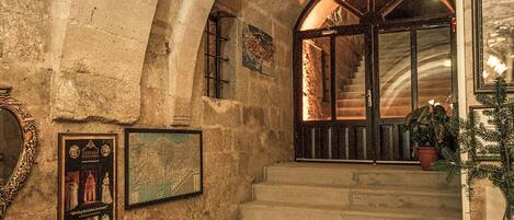 Una escalera de piedra conduce a un majestuoso arco de entrada, con cuadros en las paredes y un jarrón grande en el suelo.