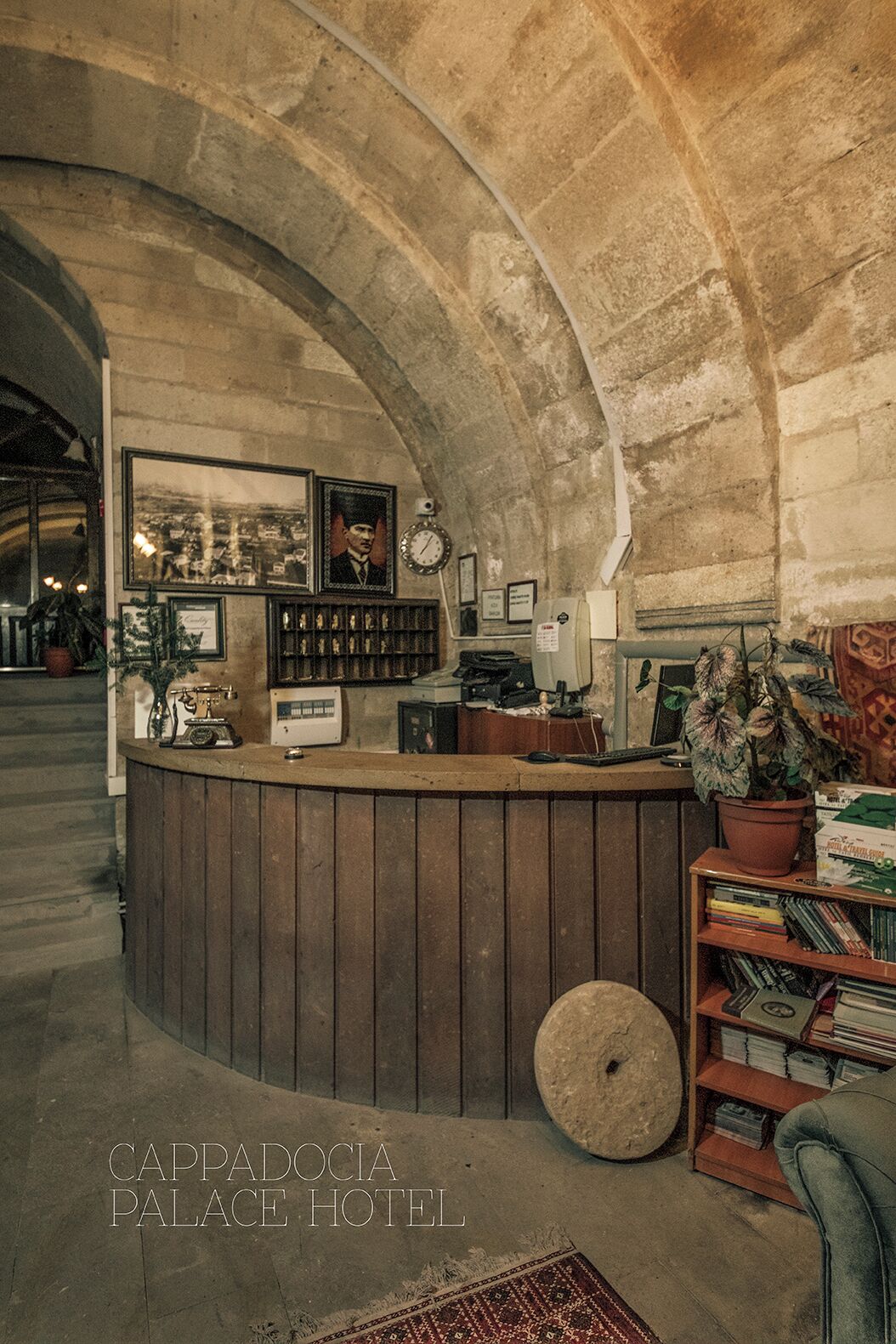 A reception area with a curved stone arch, wooden reception desk, framed photographs, a clock, and a potted plant.