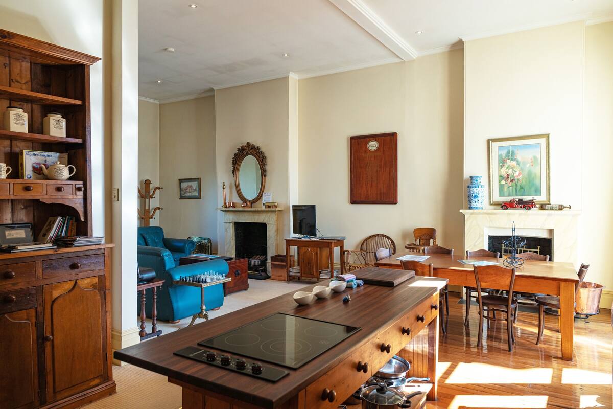 A spacious living room with a fireplace, a large wooden dining table, and a blue sofa.