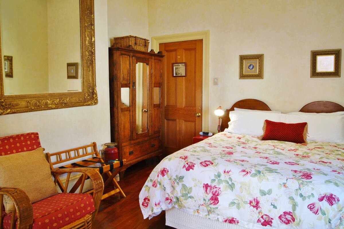 A bedroom with a floral bedspread, wooden furniture, and a large mirror.