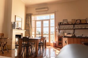 A dining area with a wooden table and chairs, a fireplace, and a large window with curtains. - Fire Station Inn (North Adelaide)