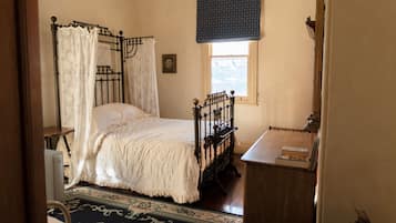 Un dormitorio con una cama con dosel, una mesita de noche de madera y una ventana con un visillo azul.