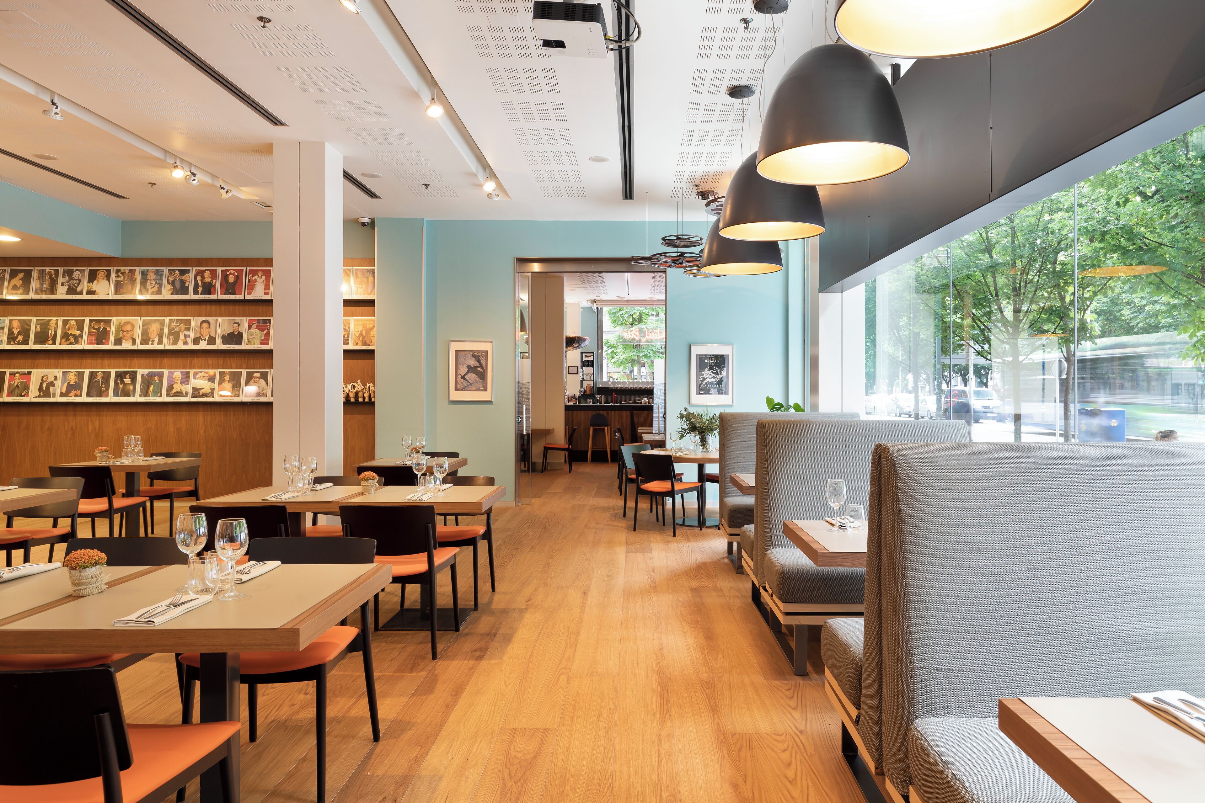 Un restaurante con mesas y sillas de madera, una zona de bar y una pared con cuadros enmarcados.