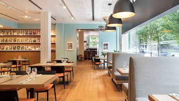 Un restaurante con mesas y sillas de madera, una zona de bar y una pared con cuadros enmarcados.