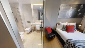 A modern hotel room with a glass partition separating the bathroom and bedroom.