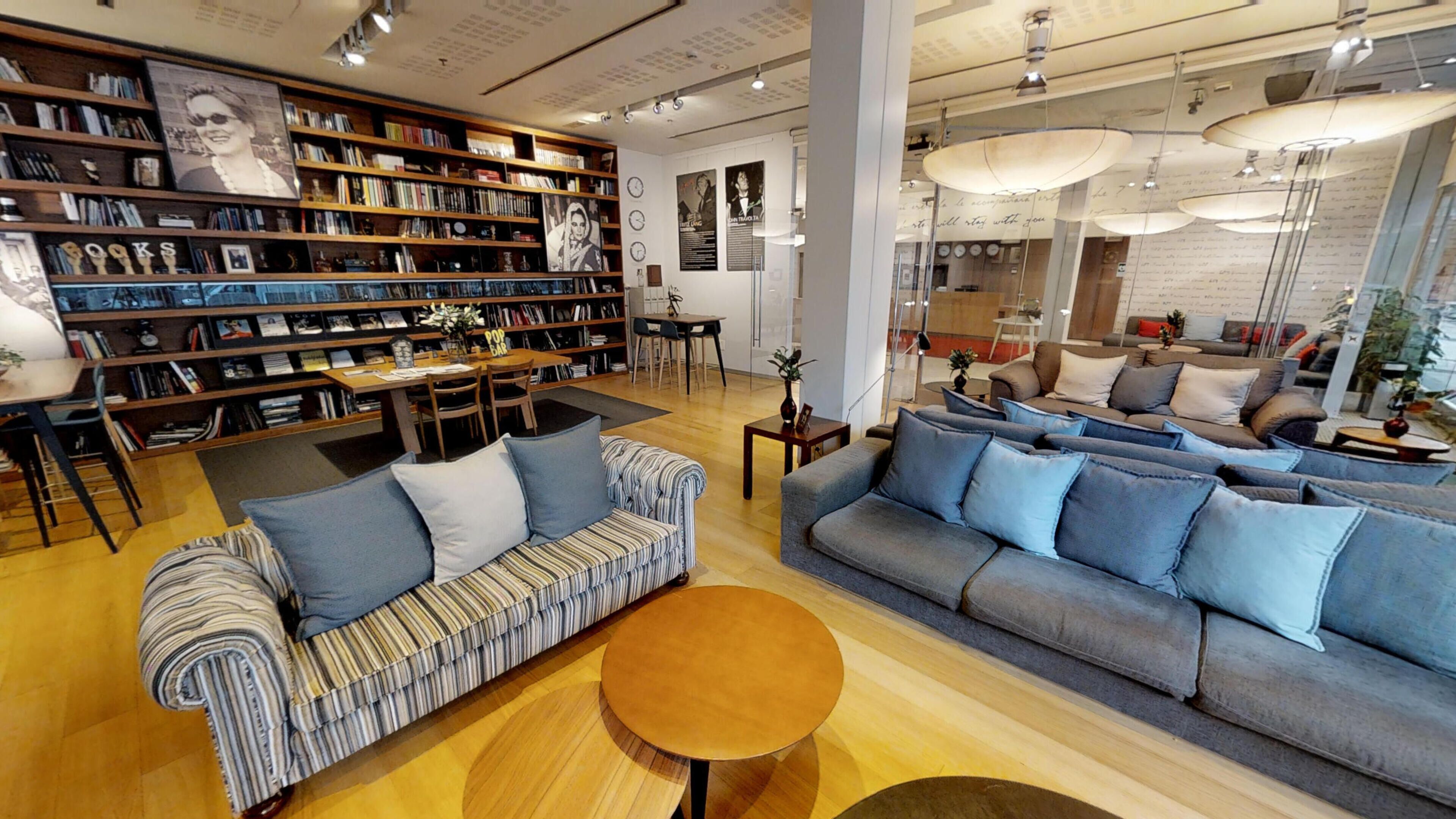 Una sala de estar moderna con un sofá, un sillón a rayas y una mesita de centro. Hay una estantería llena de libros y un comedor con una mesa y sillas.