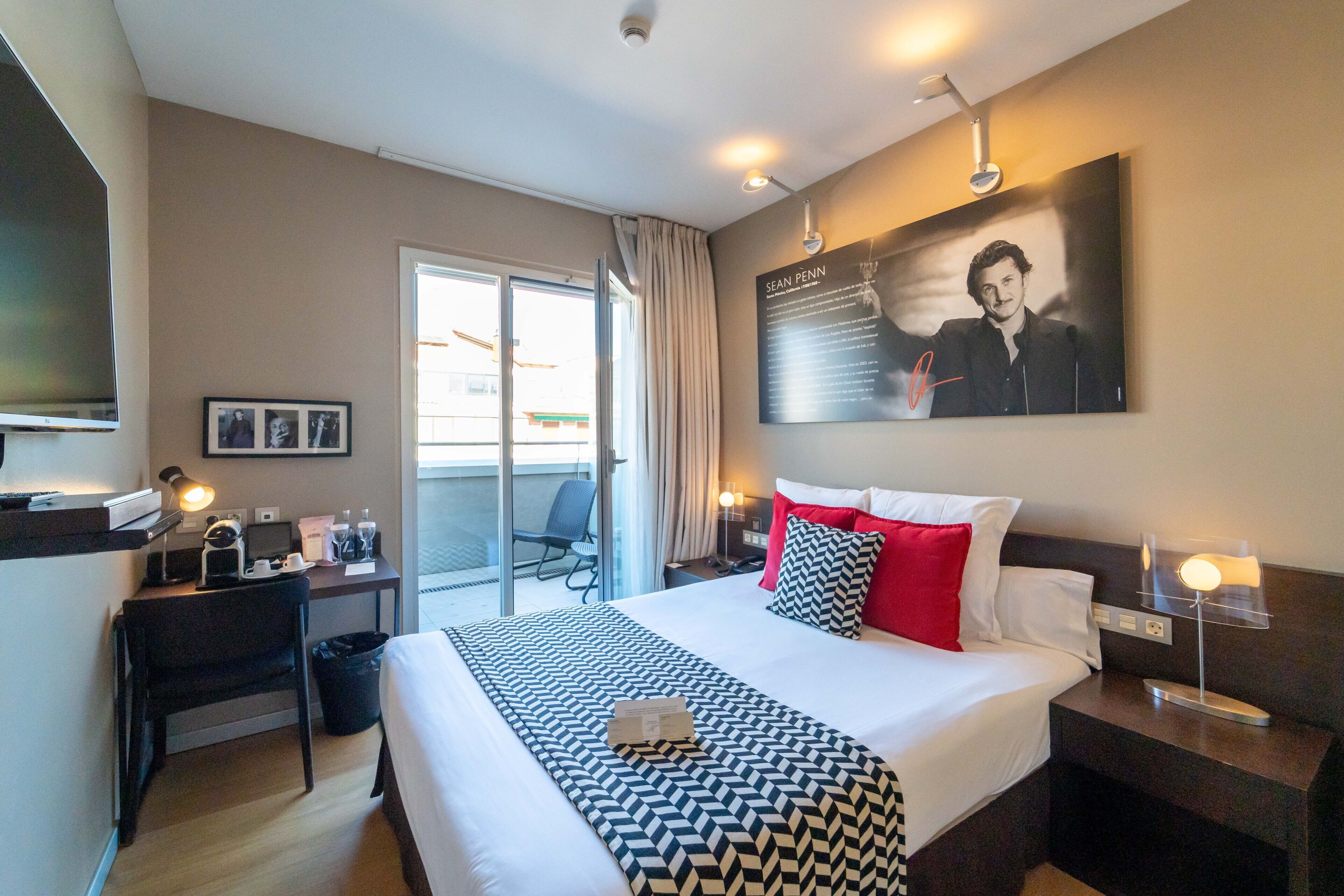 A hotel room with a large bed, a desk with a computer, a chair, a TV, and a window with curtains.