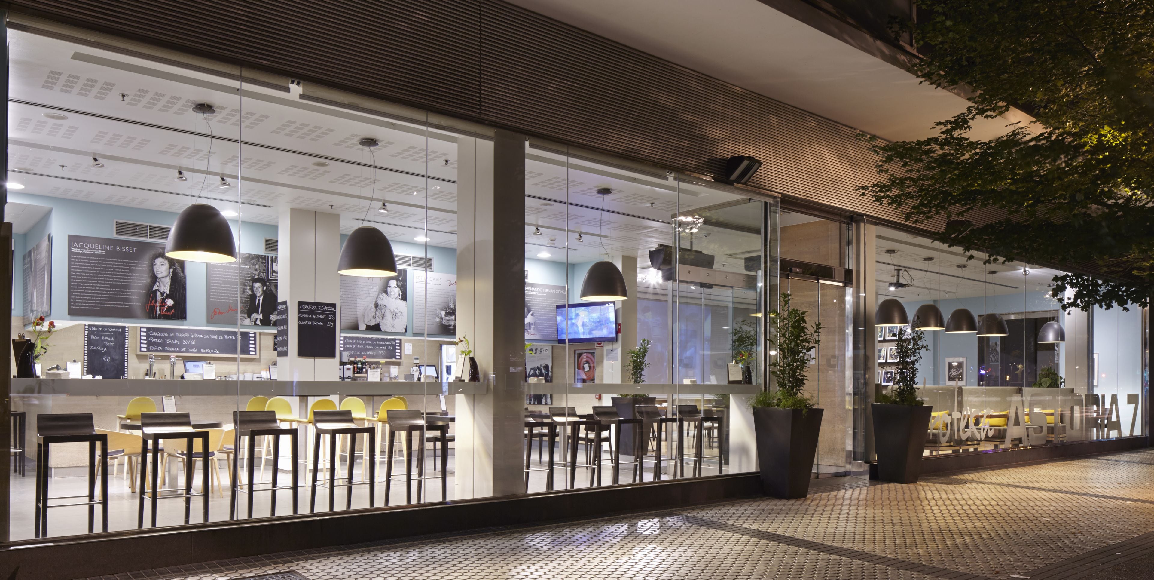 A modern cafe with large windows, indoor seating, and pendant lighting.