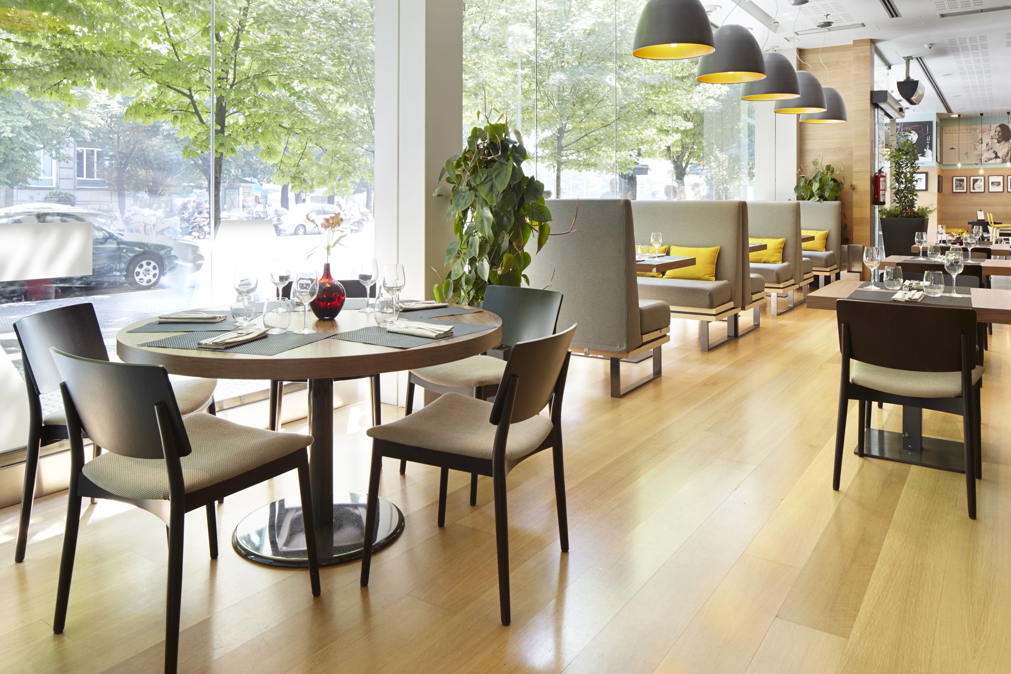Een modern restaurant met ronde tafels, comfortabele zitmogelijkheden en grote ramen met uitzicht op de straat.