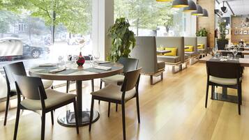 Een modern restaurant met ronde tafels, comfortabele zitmogelijkheden en grote ramen met uitzicht op de straat.