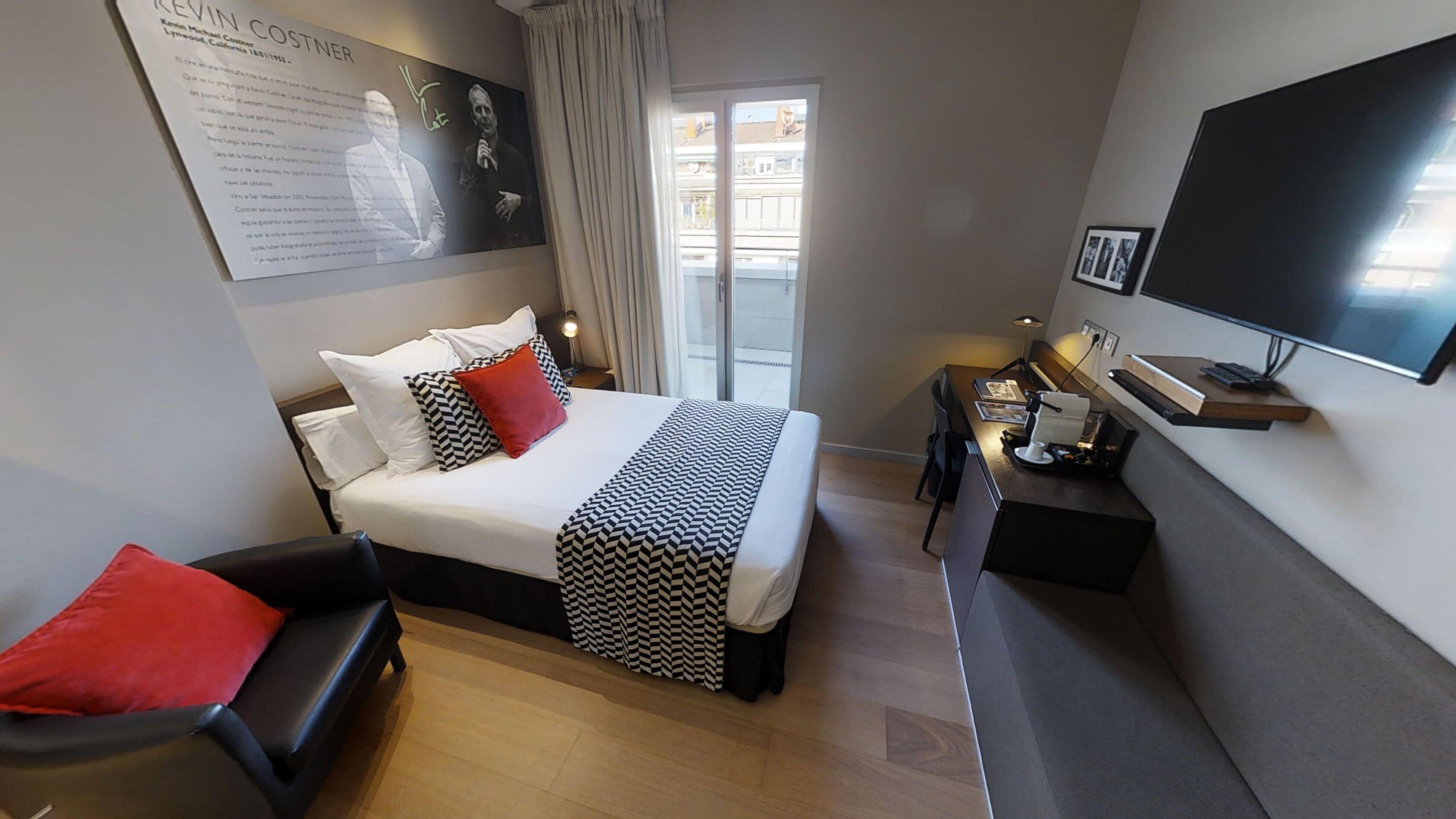 A hotel room with a bed, a desk, a chair, a TV, and a window.