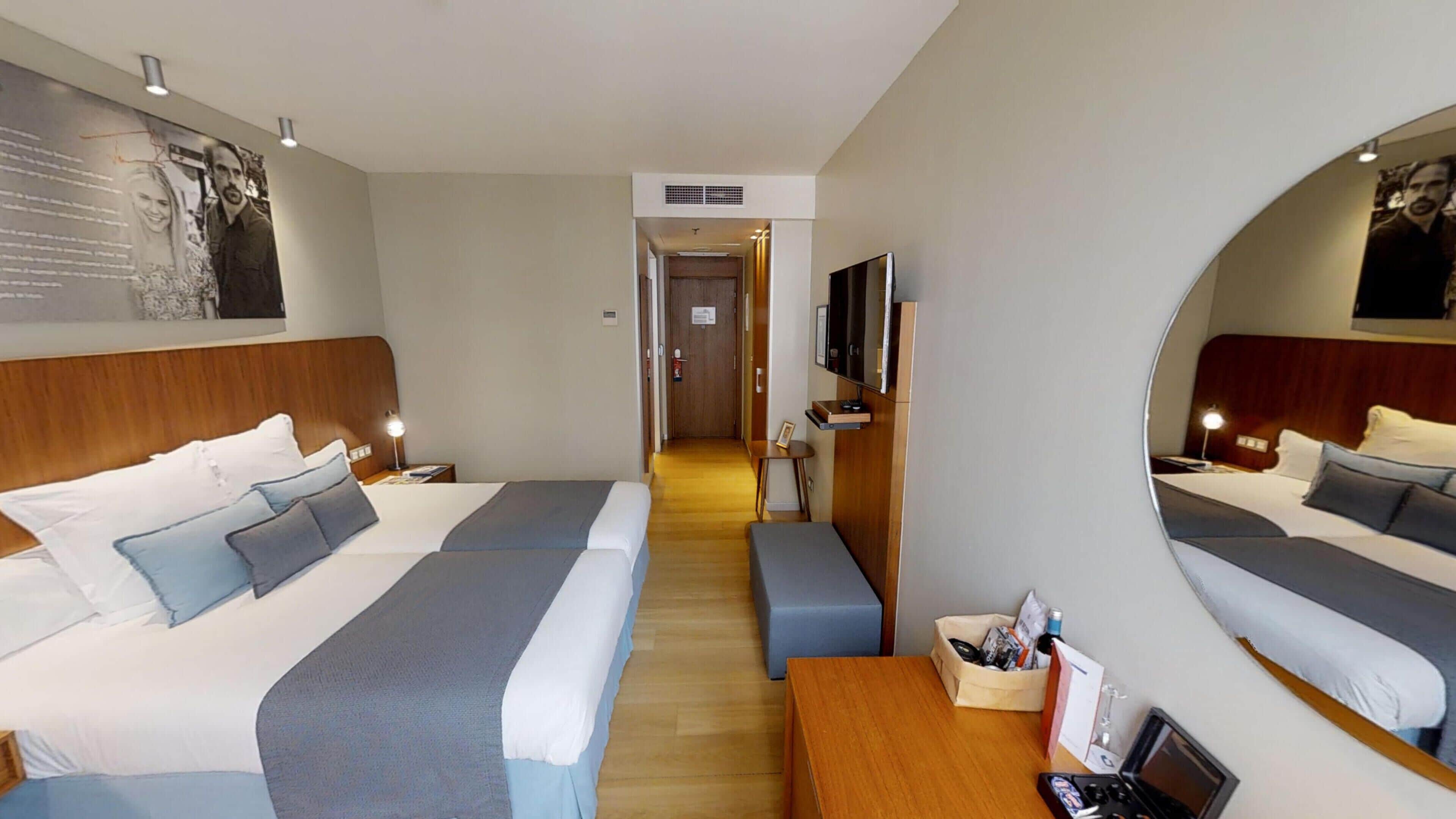 Habitación de hotel con dos camas, un cabecero de madera, un escritorio con una computadora portátil, un televisor y un espejo.