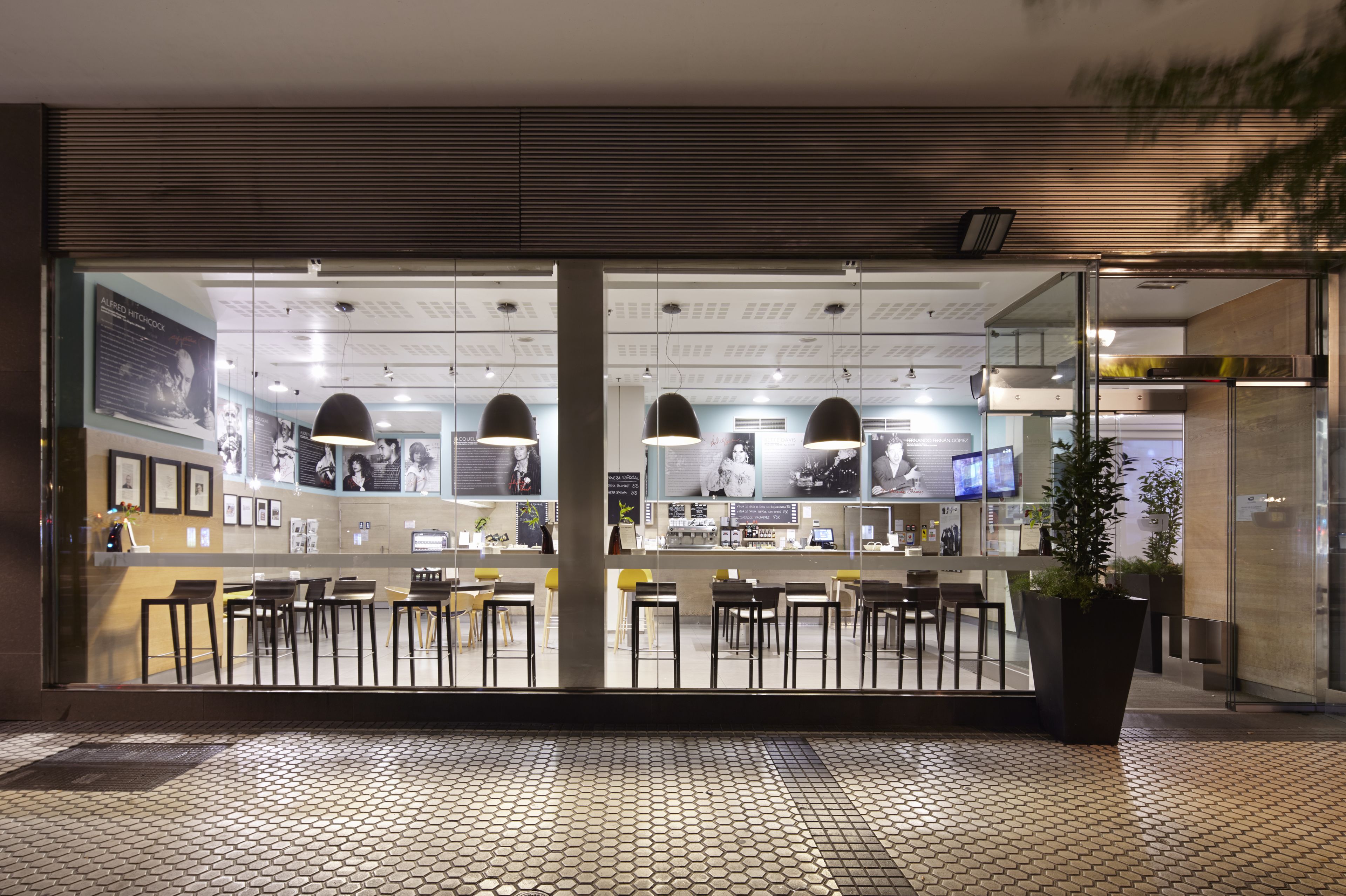 Een modern café met een betegelde vloer, glazen scheidingswanden en zwarte hanglampen.