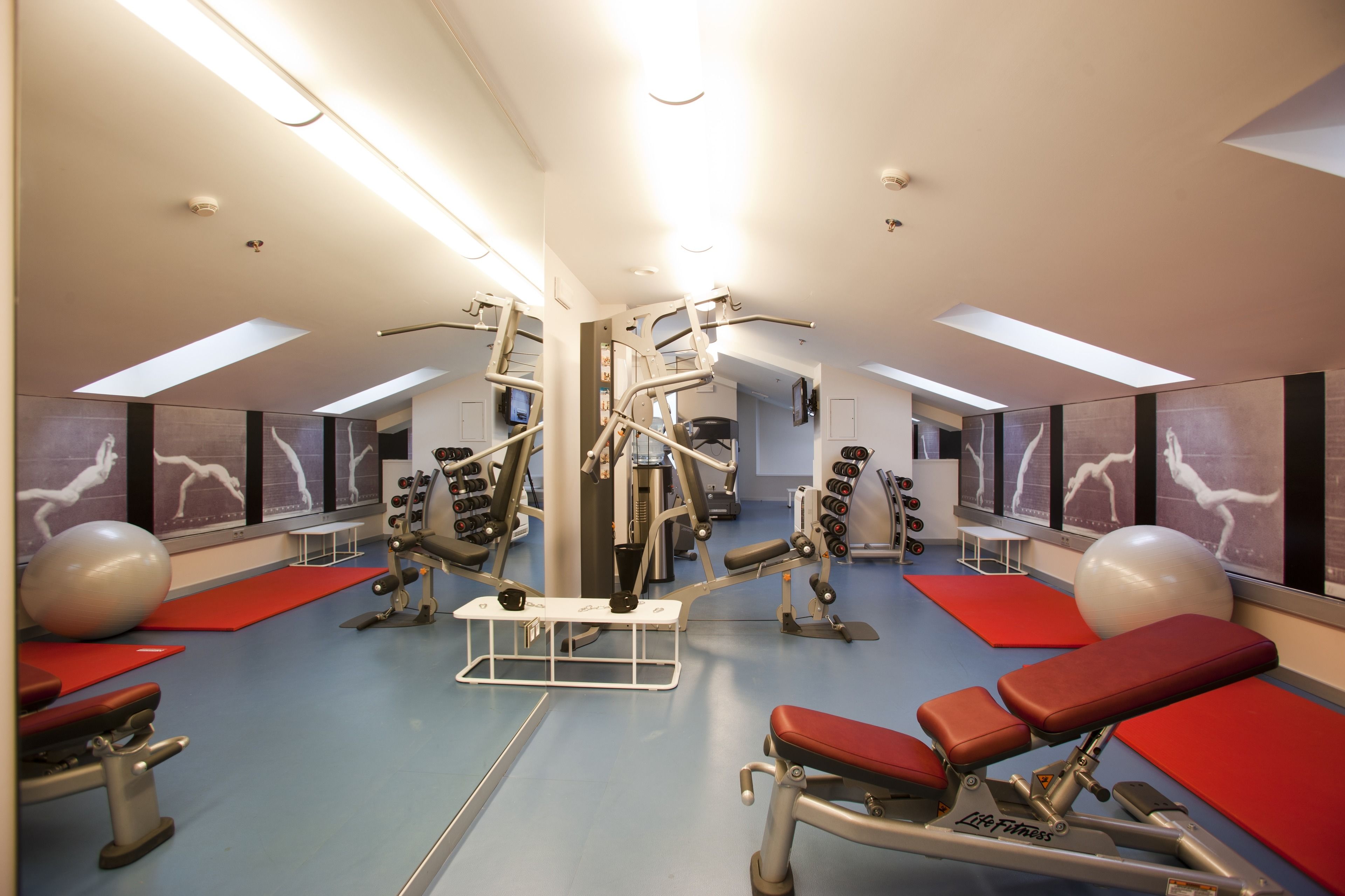 A gym with exercise equipment, red mats, and large windows.