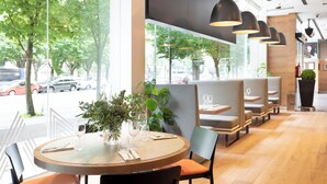 A restaurant with round tables, cushioned chairs, pendant lighting, and large windows overlooking a street. - Zinema7 (San Sebastián)