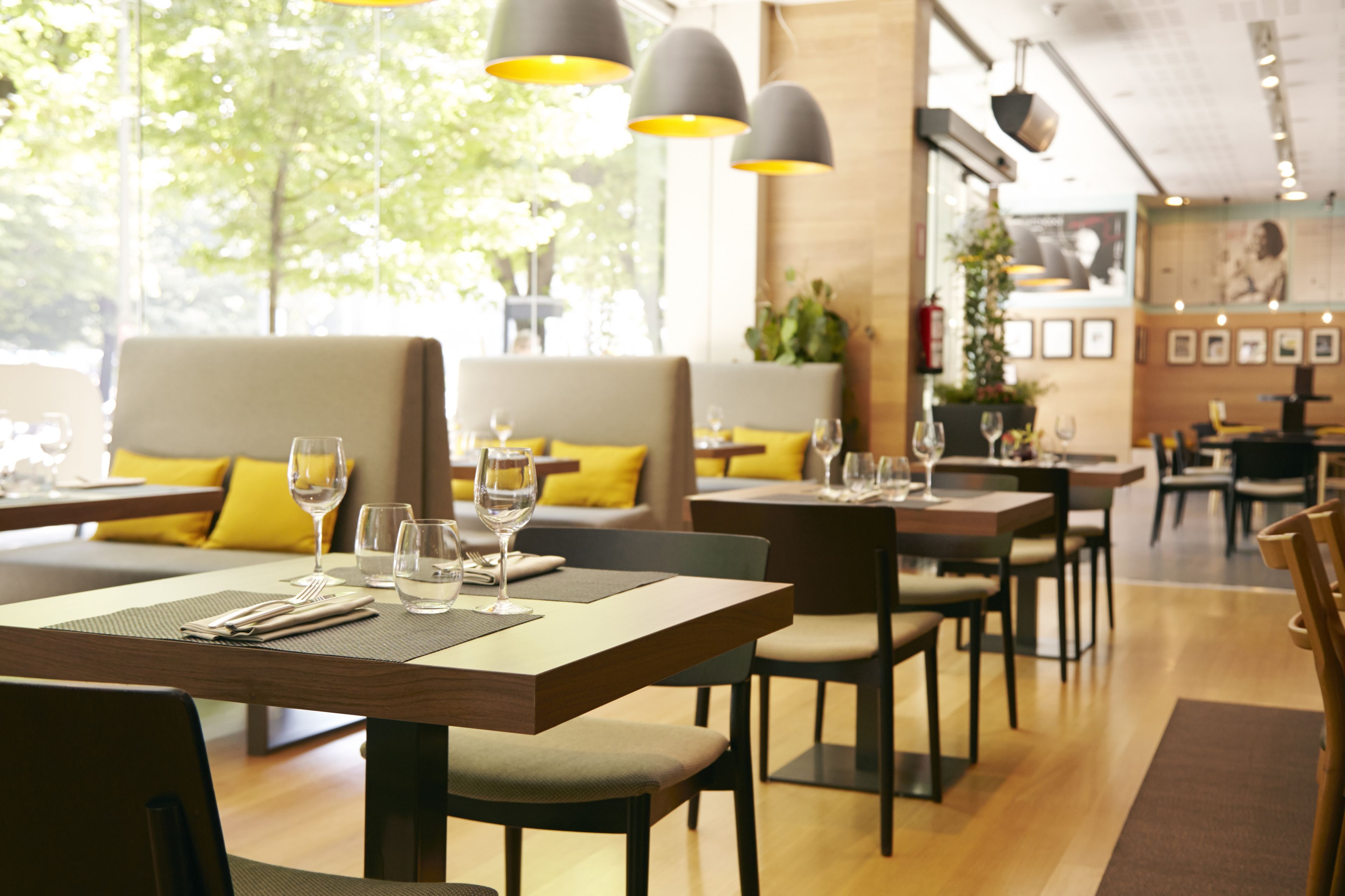 A restaurant with tables set for dining, featuring a mix of seating arrangements and a view of trees outside.