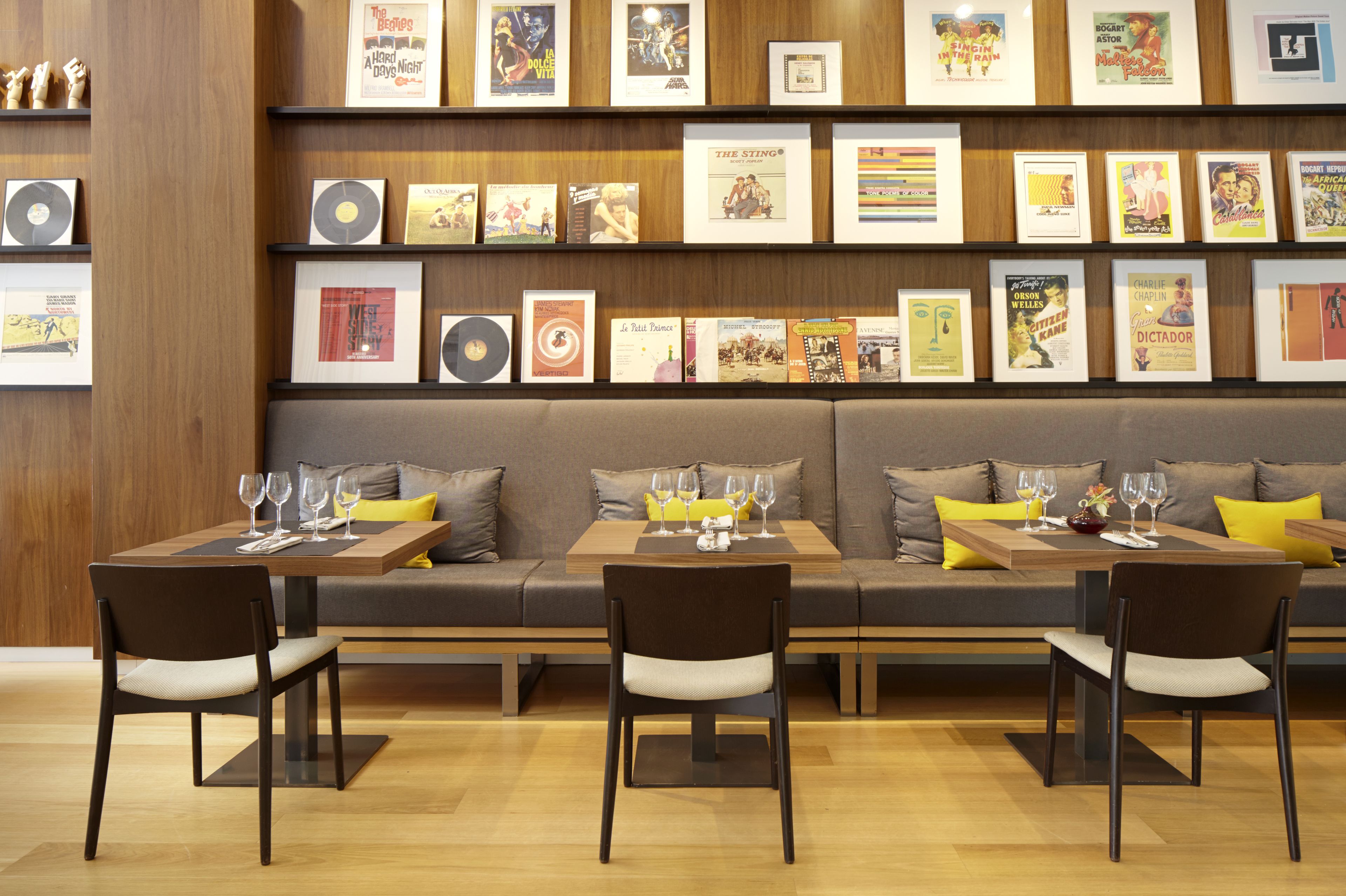 A restaurant with a long wooden bench seating area, framed pictures on the wall, and a table set with wine glasses and cutlery.