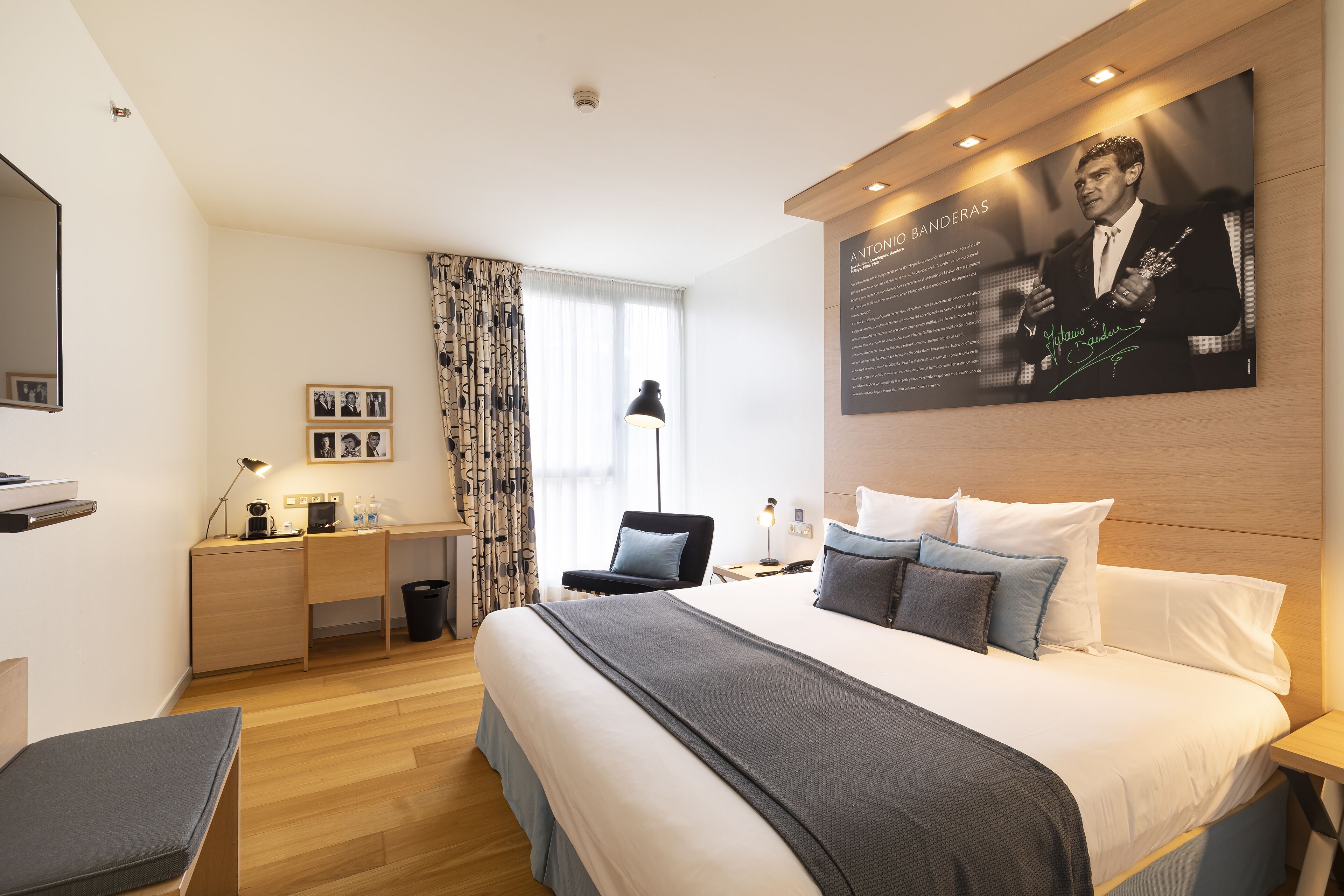 A modern hotel room with a large bed, a desk, a chair, and a flat-screen TV.
