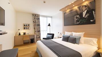 A modern hotel room with a large bed, a desk, a chair, and a flat-screen TV.