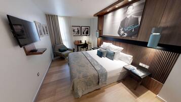 Una habitación de hotel moderna con una cama grande, un escritorio, una silla, un televisor y un cuadro colgado en la pared.