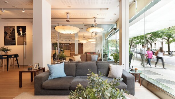 A modern interior with a grey sofa, wooden coffee table, and large windows offering a view of the street. - Zinema7 (San Sebastián)