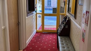 Un couloir avec un tapis rouge, un lustre, un banc et un extincteur.