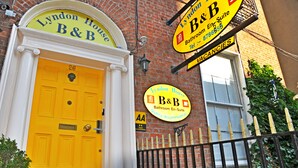 Une porte jaune avec une enseigne au-dessus indiquant : « Lyndon House, chambres d’hôtes ».
