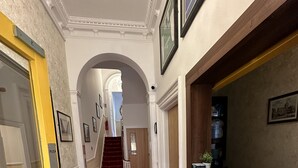 Un couloir avec un tapis rouge, des tableaux encadrés accrochés aux murs, un escalier et un banc.