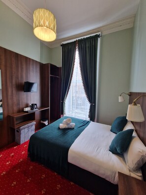 A hotel room with a bed, a television, a desk, and a window with curtains. - Lyndon House (Dublin)