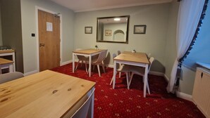Une pièce avec deux tables en bois et quatre chaises, une moquette rouge, une porte en bois et un miroir au mur.