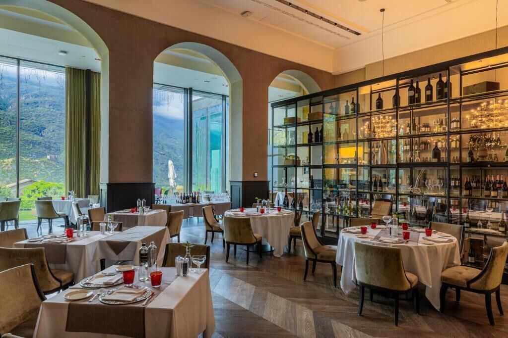 Un restaurante con mesas redondas, sillas y una estantería para vinos.