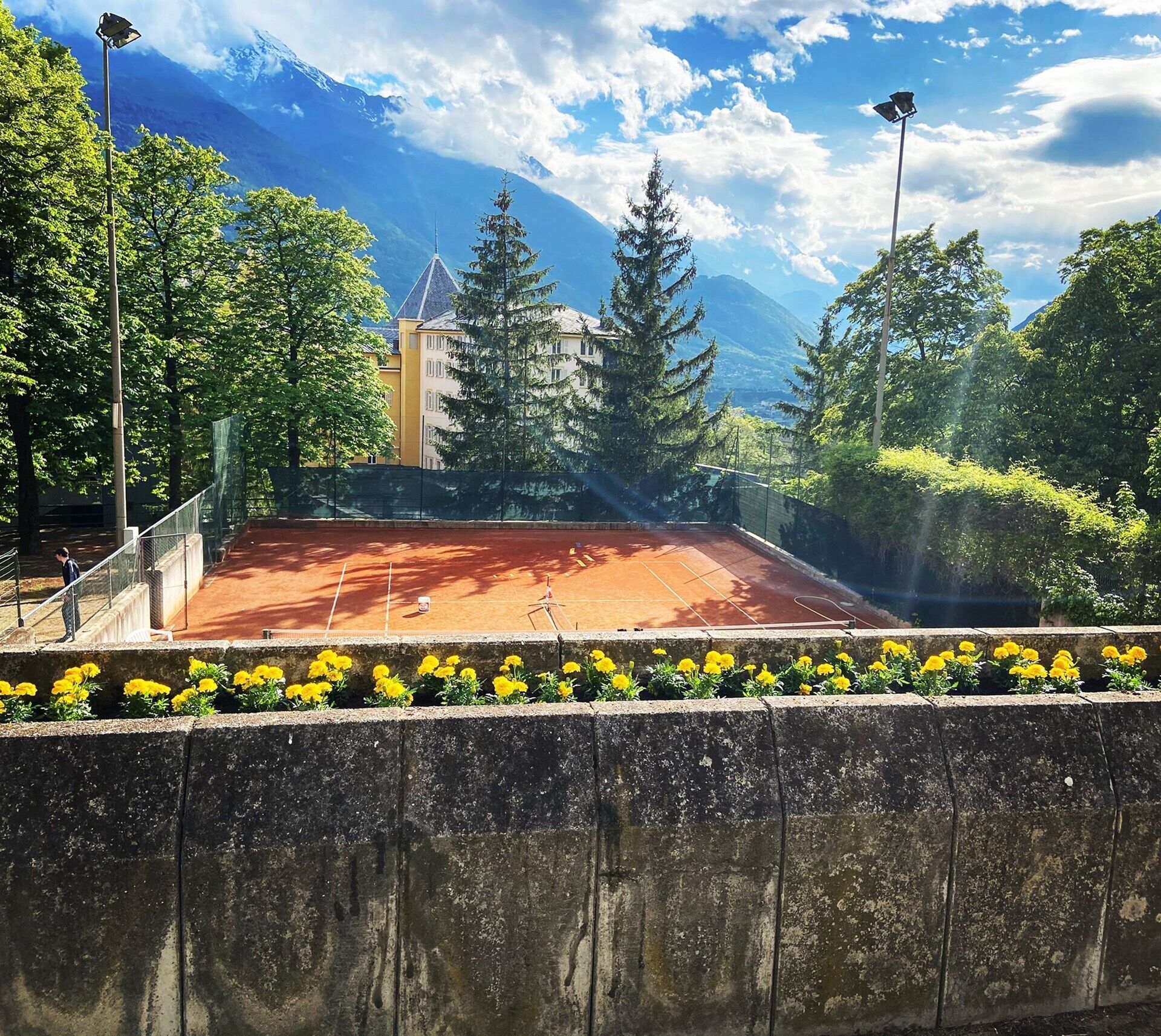 Un court de tennis avec un filet, entouré d’arbres et avec une chaîne de montagnes en arrière-plan.