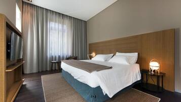 A hotel room with a large bed, a TV, a bedside table with a lamp, and a window with curtains.