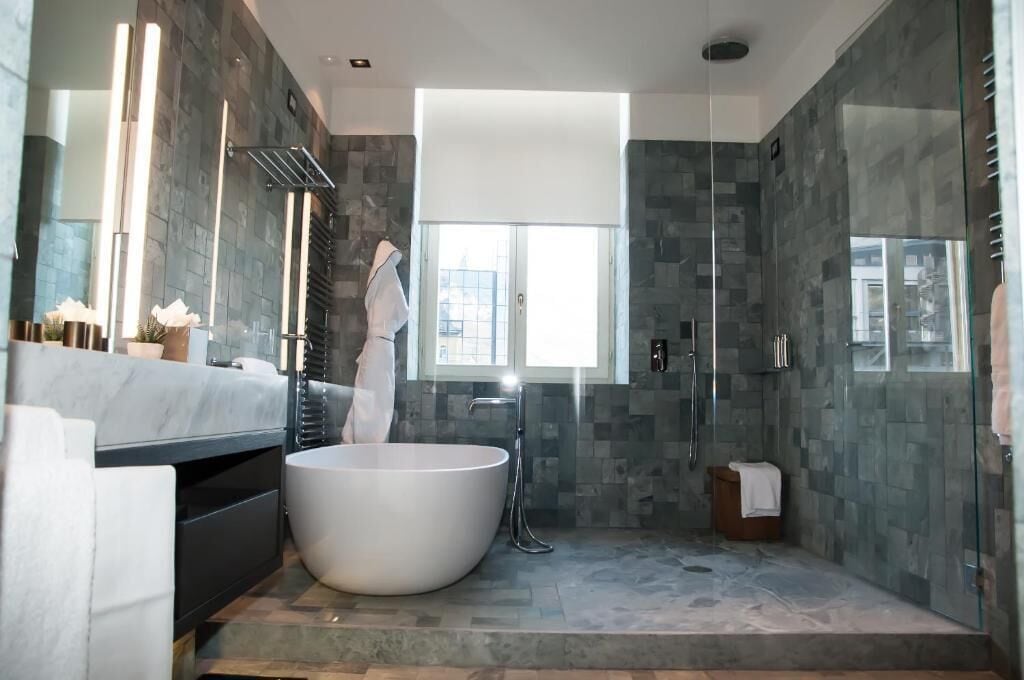 Un baño moderno con una bañera independiente, una ducha con mampara de vidrio y un amplio ventanal que proporciona luz natural.