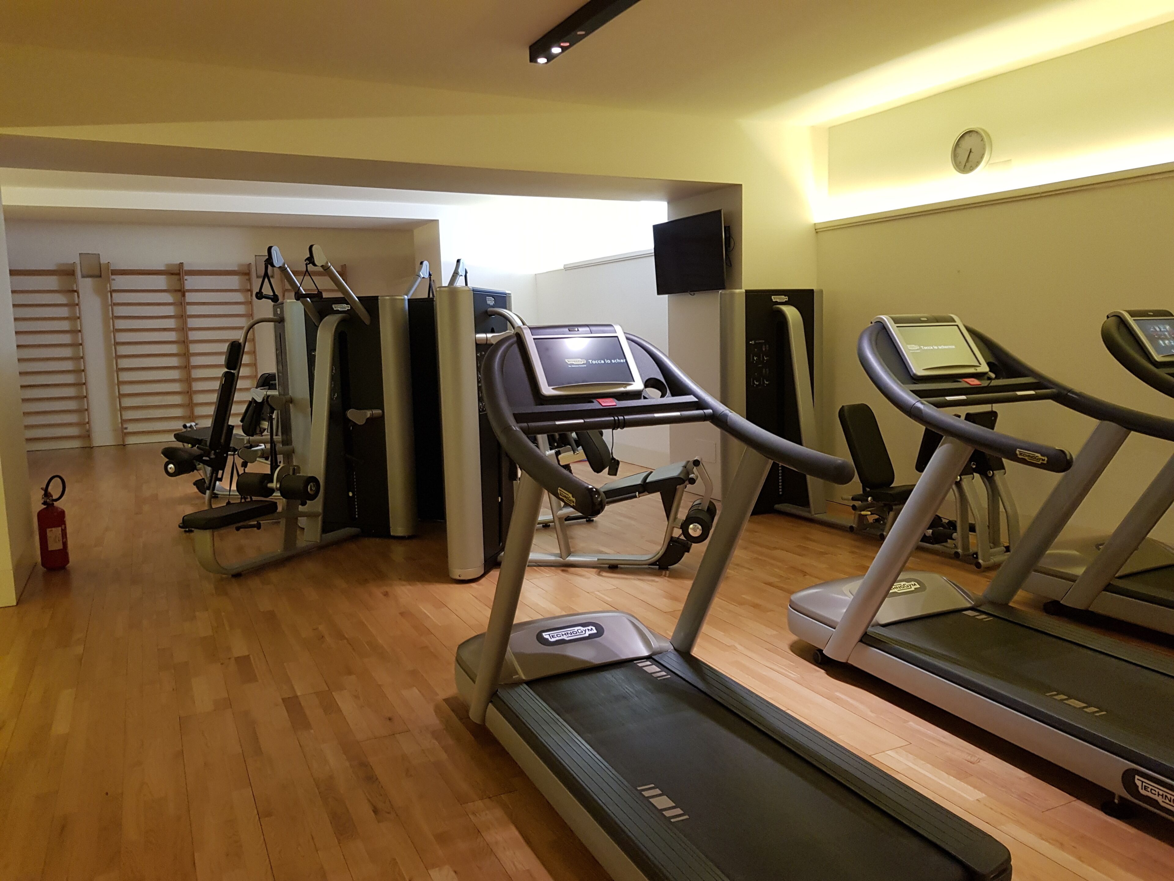 Un gimnasio con cintas de correr, máquinas de pesas y una televisión montada en la pared.
