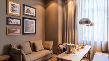 A cozy living room with a sofa, a dining table with a lamp, and framed certificates on the wall.