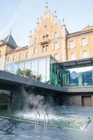 Un edificio moderno con fachada de vidrio y zona de piscina con vapor saliendo del agua.